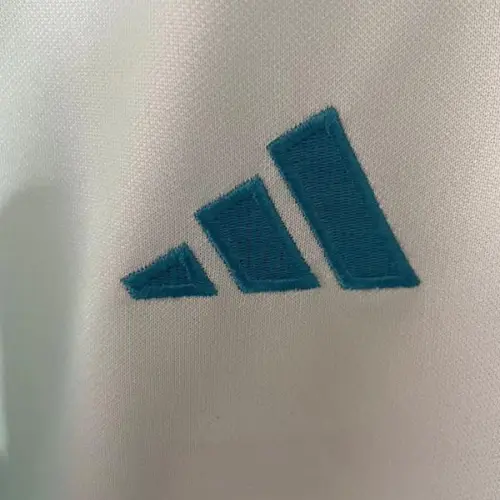 Camisa reserva Munster 24/25, azul claro com listras verticais verde-água e texto em irlandês.